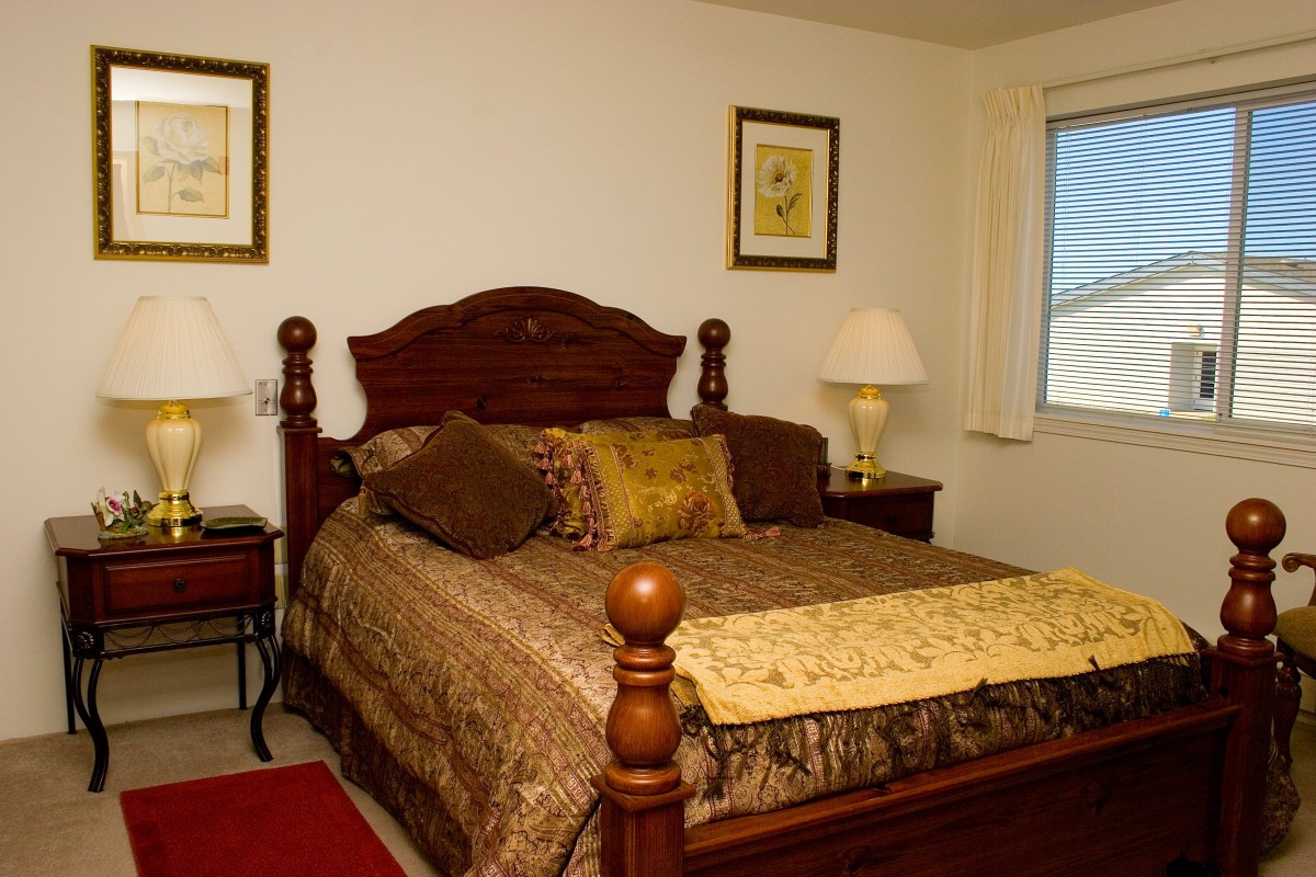A cozy bedroom featuring a wooden bed with decorative pillows and a matching lamp on the bedside table.