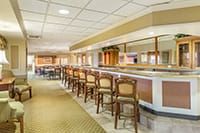 An empty bar interior with a row of wooden chairs lined up along the counter.