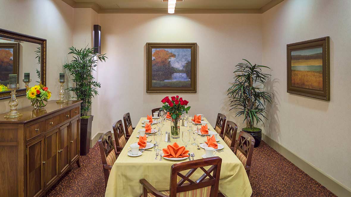 A elegantly set dining table with red flowers, surrounded by chairs and decorated with art and plants.