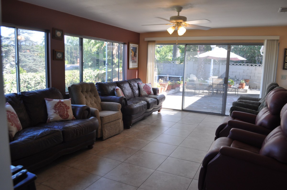 A spacious living room with tiled flooring, featuring a sofa and armchairs facing large windows and a sliding glass door leading to an outdoor area.