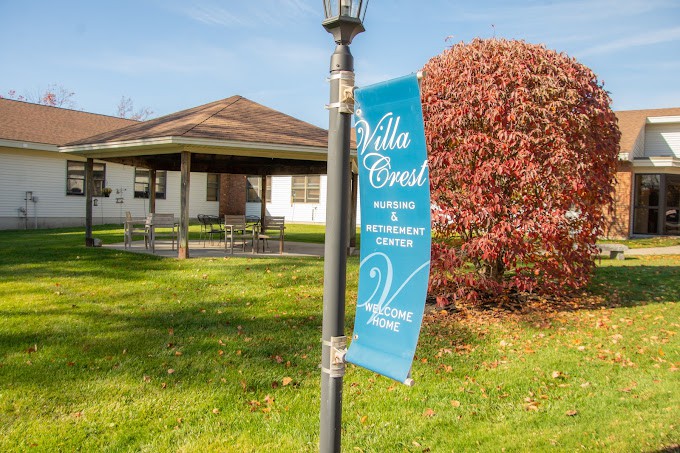 A banner reading 'Villa Crest' is attached to a lamppost, with a building and autumn foliage in the background.