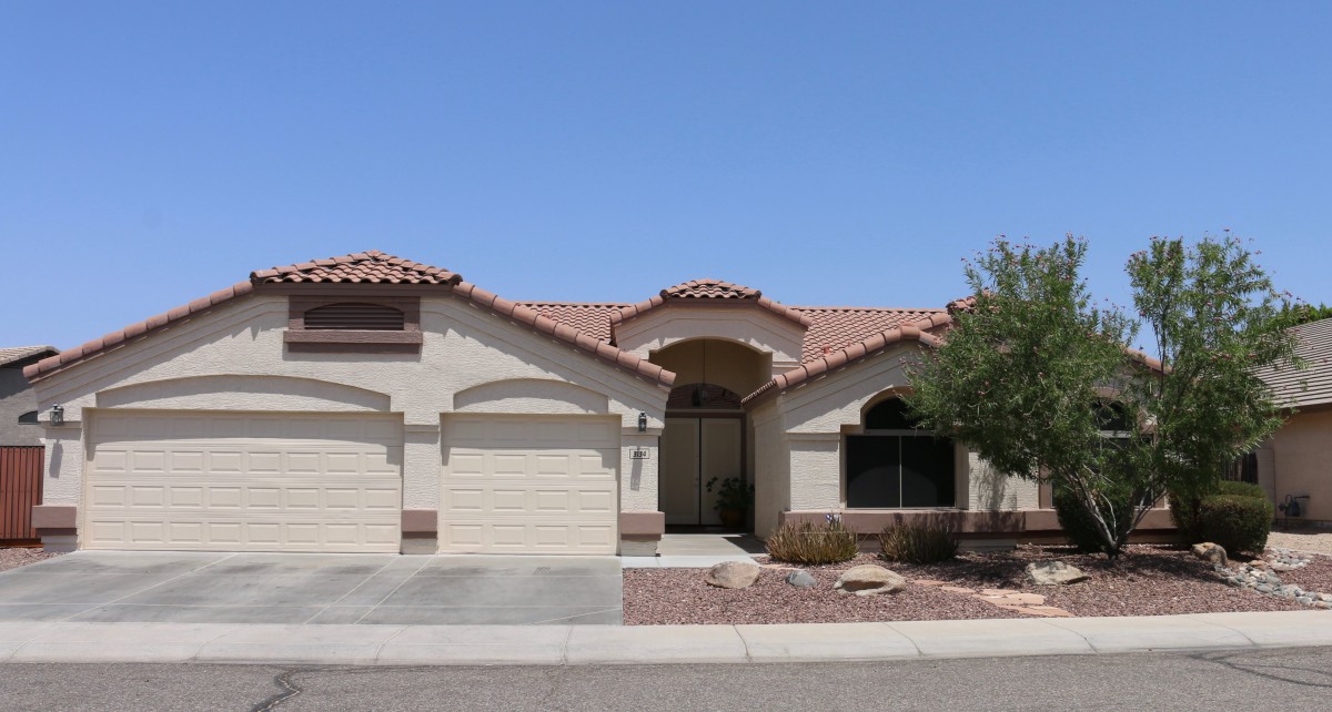 A single-story suburban house with a desert landscape and a three-car garage.