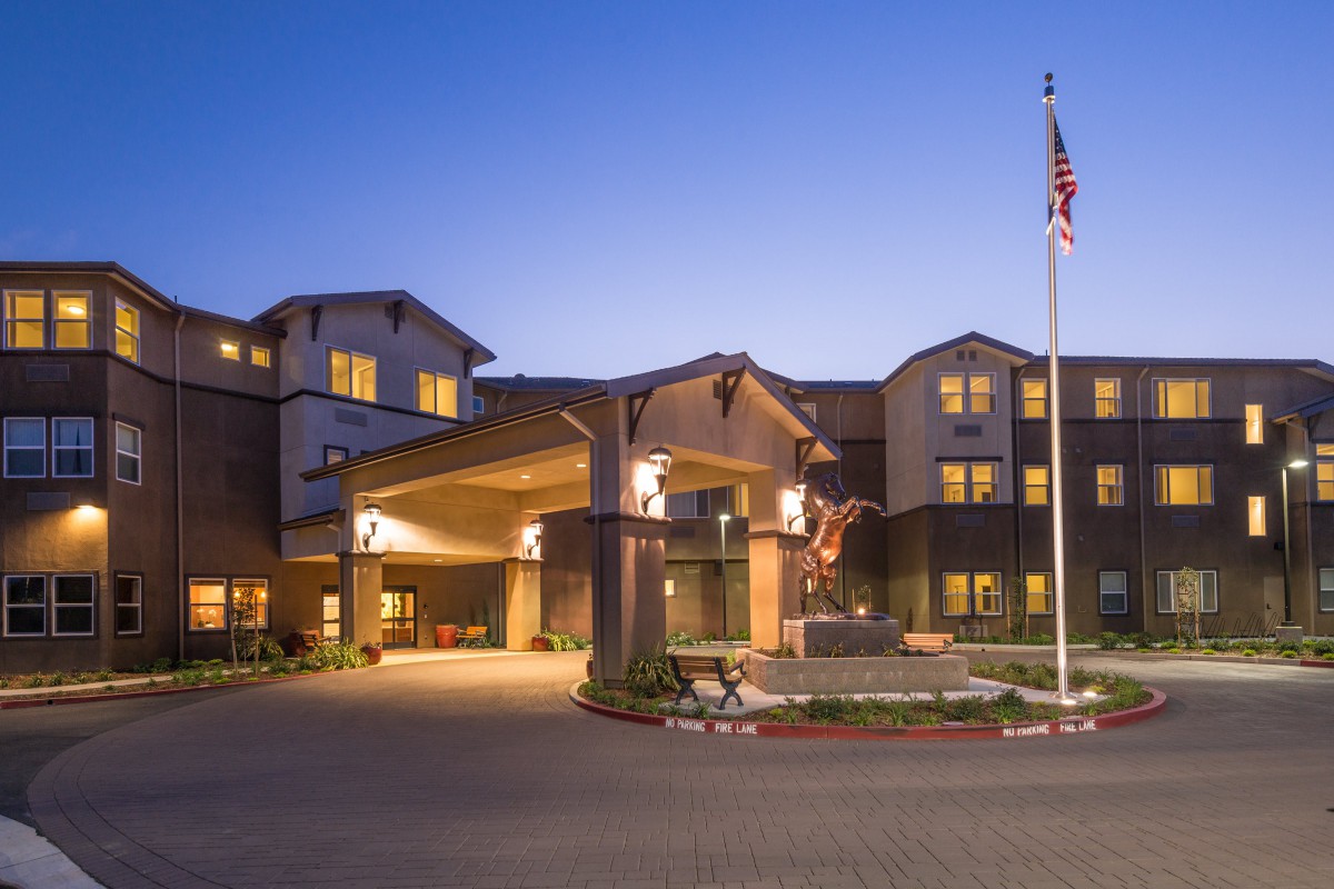 A well-lit hotel exterior at dusk with an entrance and a flagpole.