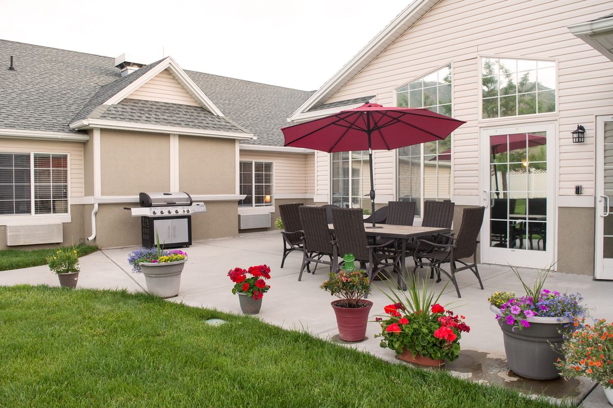 A cozy outdoor patio with a dining set, umbrella, and grill surrounded by potted plants.