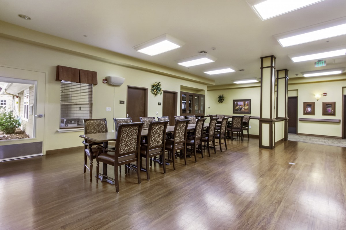 A spacious dining room with a long table and chairs, featuring a wooden floor and bright lighting.
