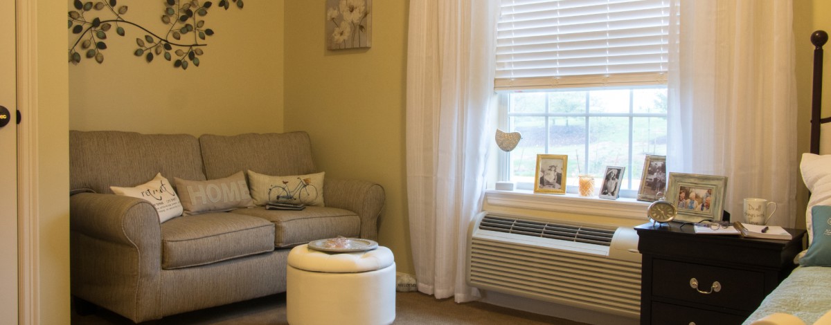 A cozy living room corner featuring an armchair, ottoman, and window with curtains.