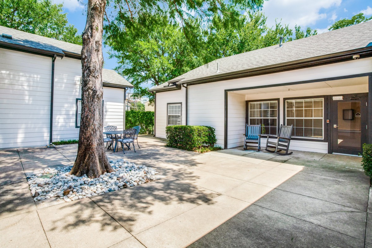 A sunny backyard patio with outdoor furniture, featuring a tree beside a house.