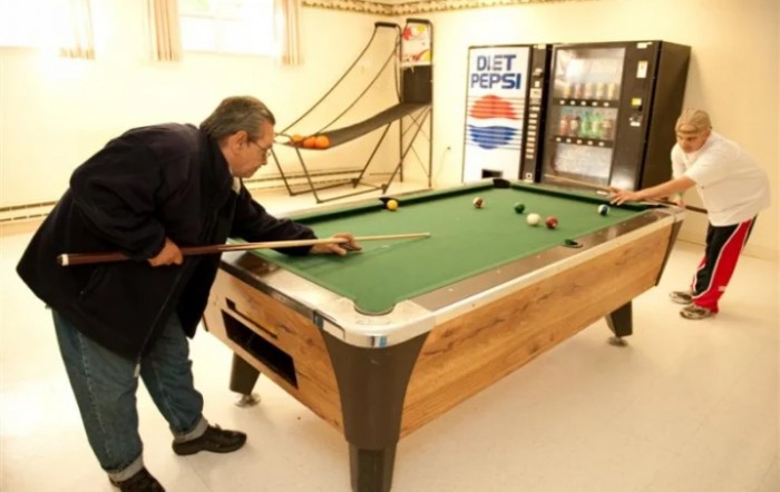A person playing billiards in a recreation room with a vending machine in the background.
