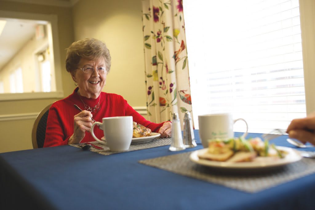 An elderly woman in a red sweater enjoying a meal at the dining table.
