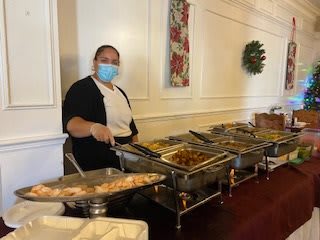 A server wearing a mask is standing next to a buffet setup indoors.