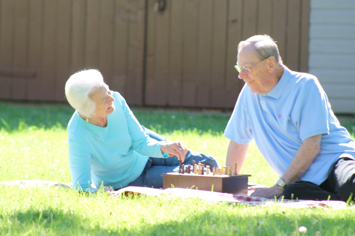 An elderly couple enjoys a game of chess on a sunny day in the park.