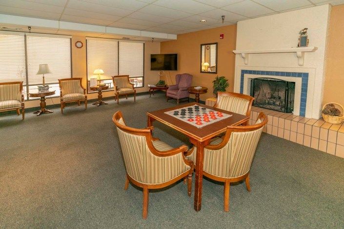 A cozy lounge area featuring a chessboard table, comfortable chairs, a fireplace, and a television.