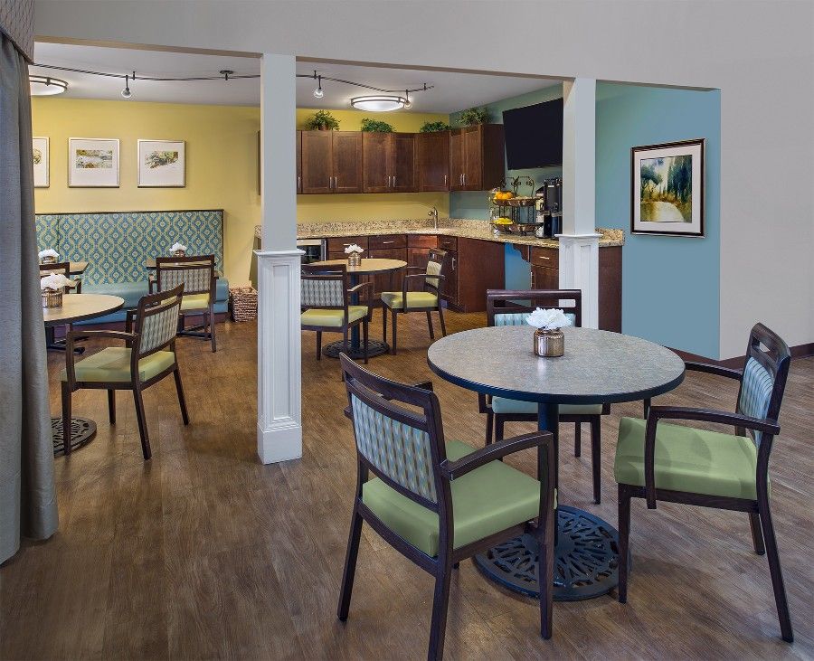 A modern cafe interior with neatly arranged tables and chairs, featuring a small kitchen area in the background.