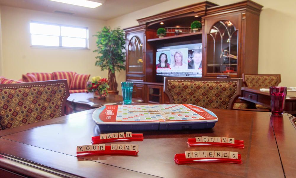 A cozy living room features a Scrabble game in progress on a table, with a television and comfortable seating arrangements.