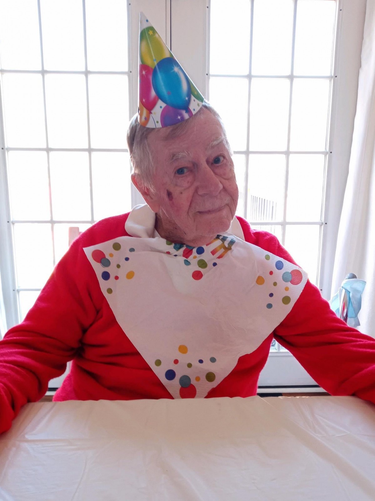 A senior person dressed for a birthday celebration with a party hat and festive bib.