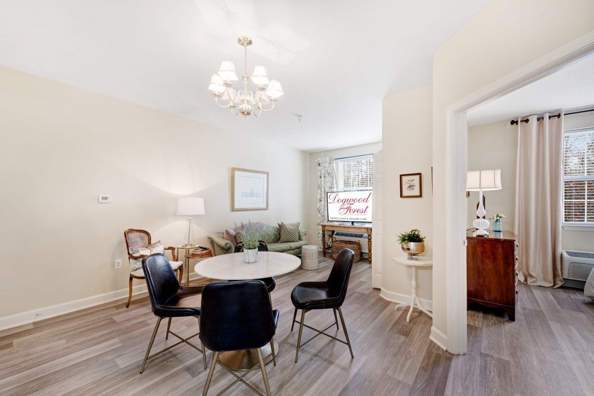 A cozy living room with a dining area featuring a round table, four black chairs, and elegant lighting.