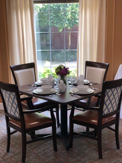 A dining table elegantly set for four, positioned near a large window with curtains.