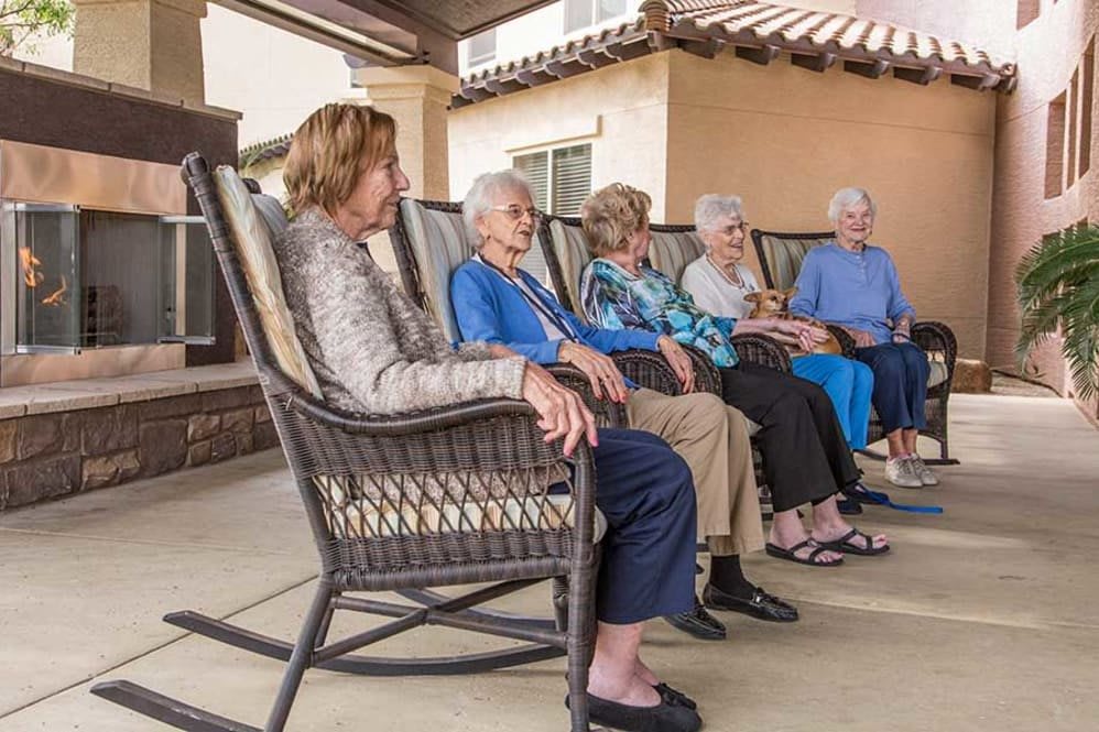 A group of seniors sitting in rocking chairs on a porch, enjoying a social moment outdoors.