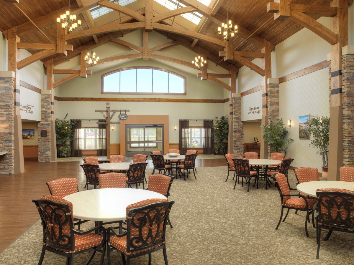 A spacious dining area with round tables, cushioned chairs, and wooden beams under a high ceiling with chandeliers.