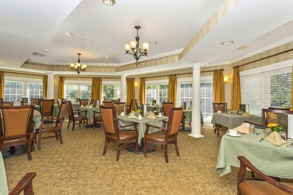 An elegant dining room with neatly arranged tables and chairs, featuring chandeliers and decorative curtains.