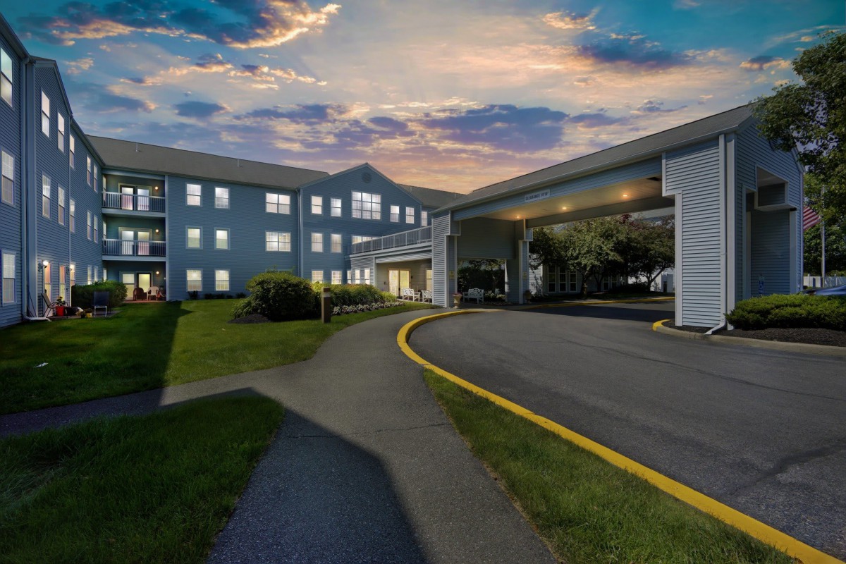 A nighttime view of a hotel entrance with a curved driveway and illuminated windows.