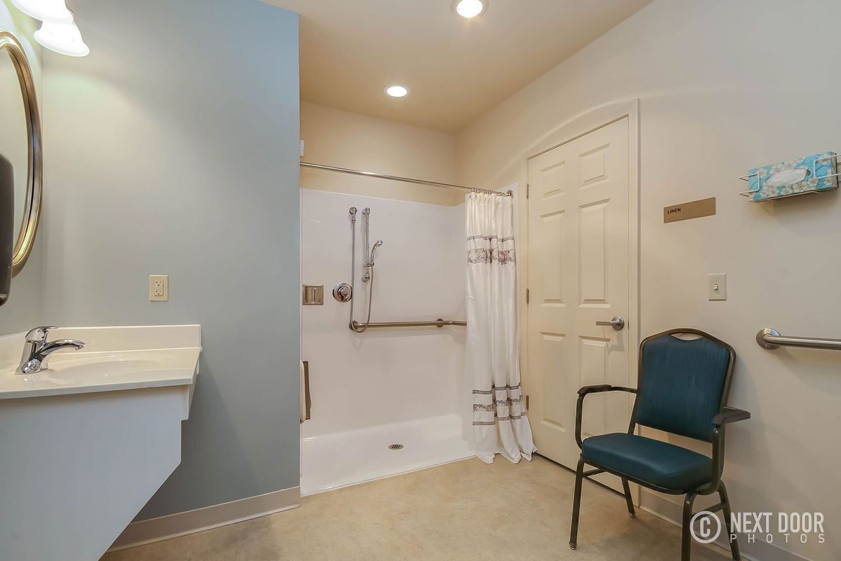 A modern and accessible bathroom featuring a walk-in shower with grab bars and a chair.