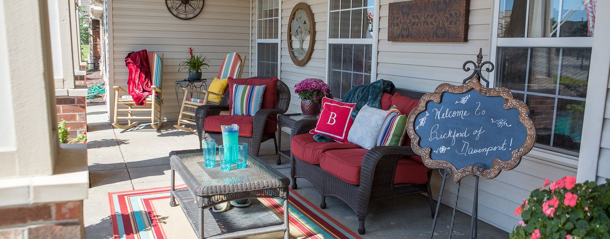 A cozy outdoor patio setup with armchairs, colorful cushions, and a small table surrounded by decorative items and plants.