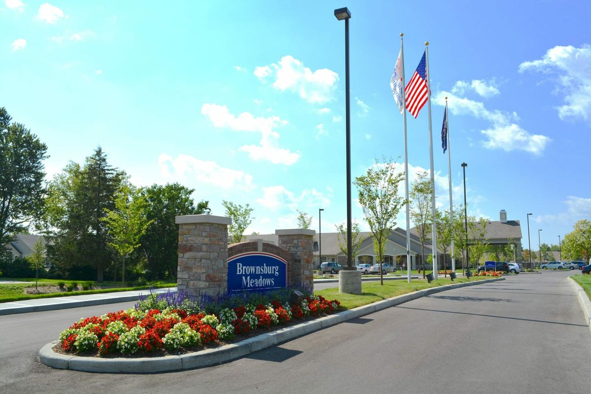 Entrance of a facility with a welcoming sign, flags, and landscaped flowers.