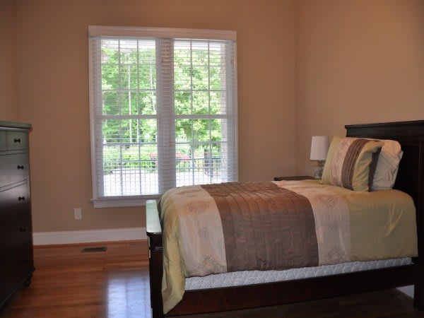 A cozy bedroom with a neatly made bed and large window allowing natural light to enter.