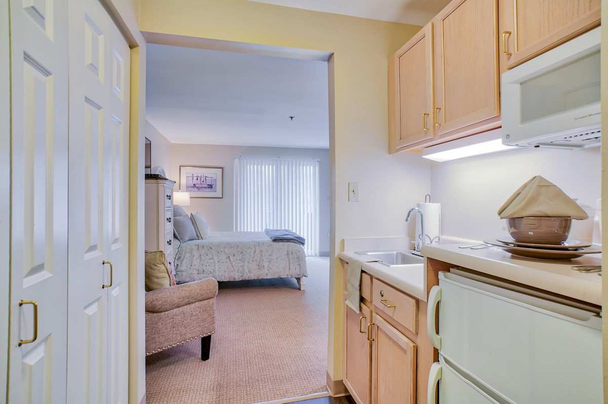 A cozy apartment interior featuring a small kitchen area leading into a comfortable living space with a bed.