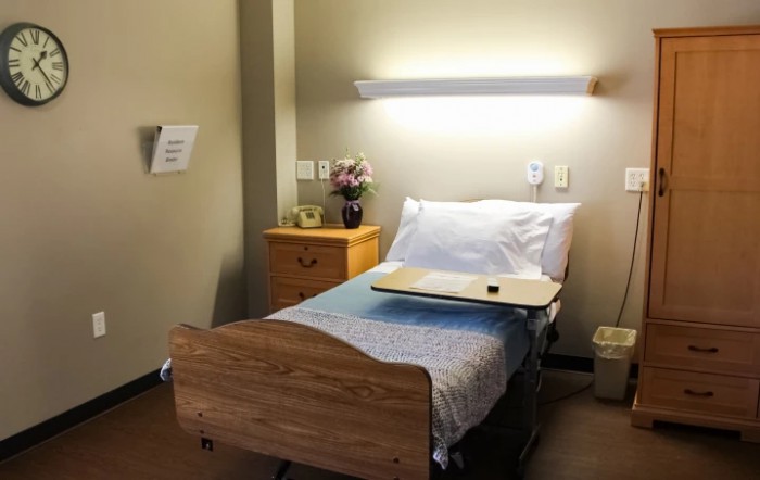 A well-lit hospital room with a single bed and wooden furniture.