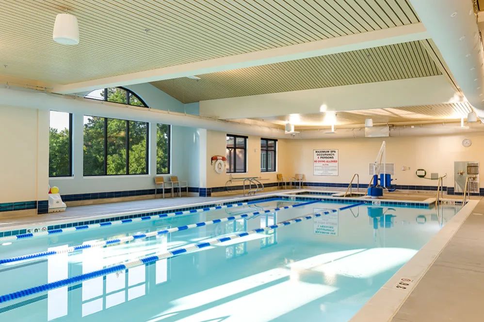 An indoor swimming pool with multiple lanes and natural light streaming in through large windows.