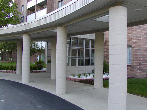 An architectural view of a modern building entrance with columns and landscaped area.