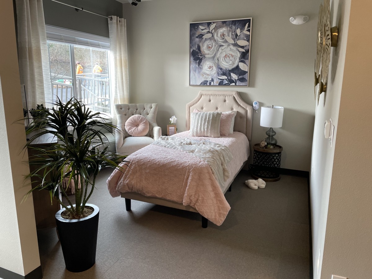 A cozy bedroom with a single bed, decorative pillows, and a potted plant by the window.