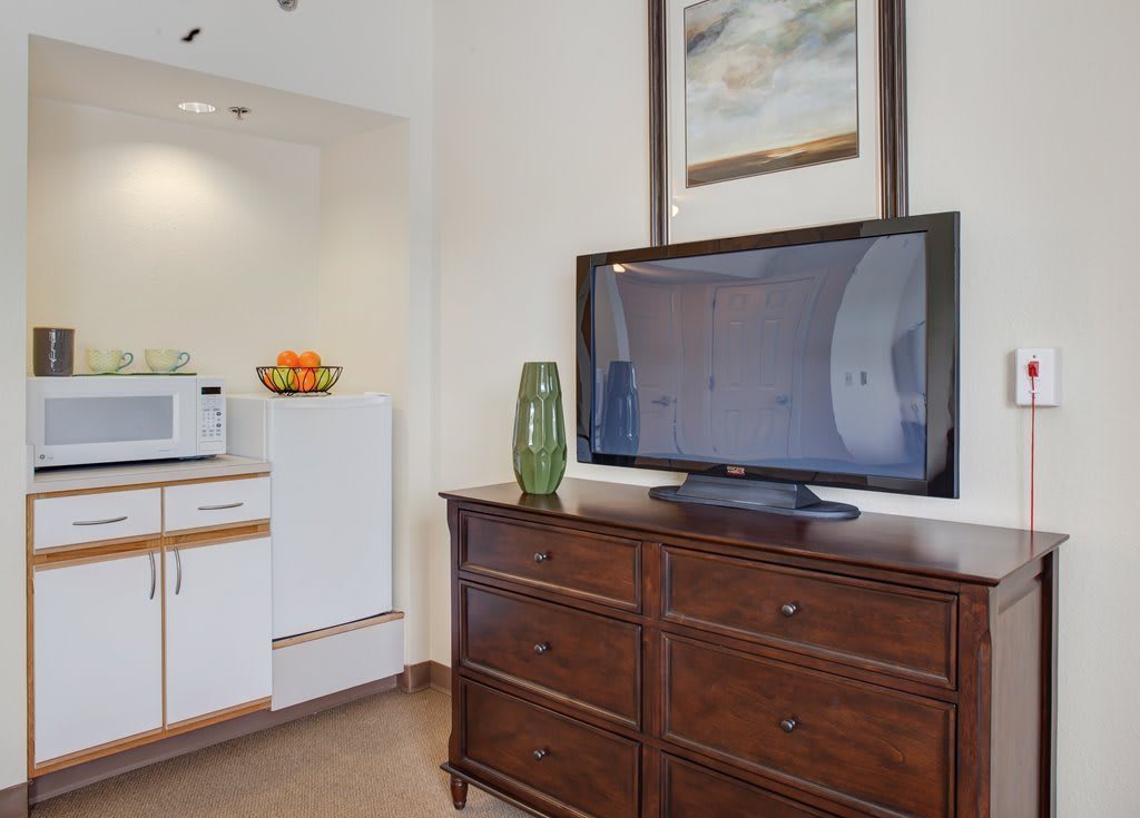 A cozy living space with a TV on a wooden dresser, adjacent to a kitchenette.