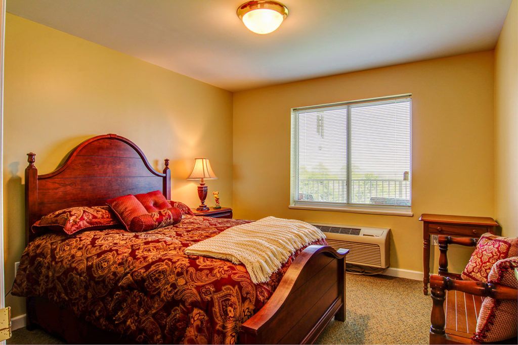 A cozy bedroom interior with a wooden bed, lamp, and window.