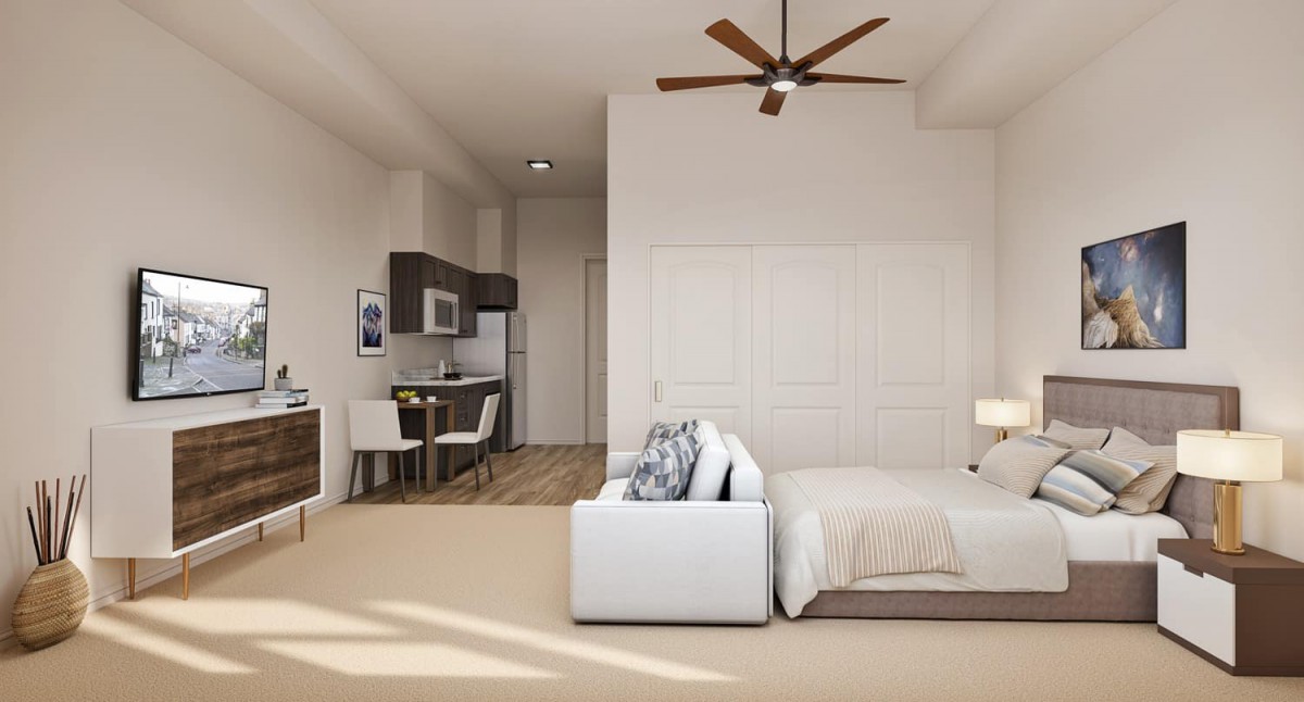 A modern studio apartment interior featuring a bed, kitchenette, and ceiling fan.