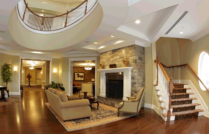 A spacious and elegant living room featuring a cozy fireplace, comfortable sofas, and a grand staircase with hardwood flooring.