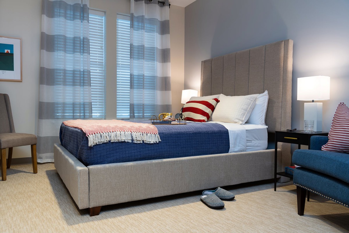 A cozy bedroom with a neatly made bed featuring pillows and a blanket, next to a nightstand with a lamp.