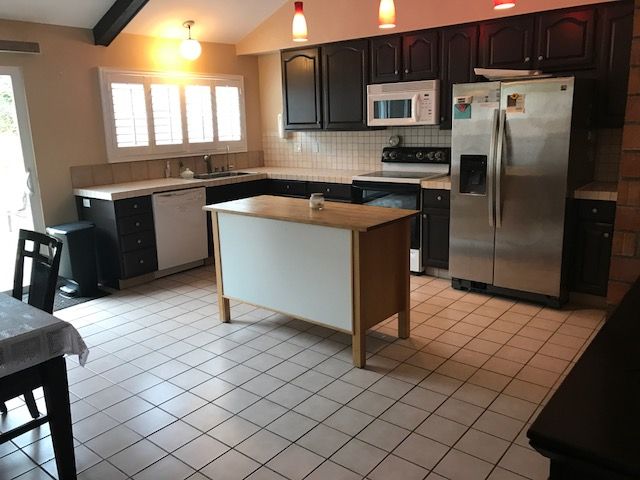 A modern kitchen with a central island, dark cabinets, and stainless steel appliances.