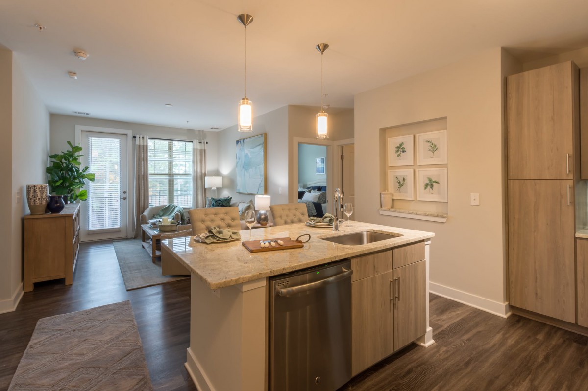 A modern open floor plan featuring a kitchen with an island and pendant lighting, leading into a cozy living room area.