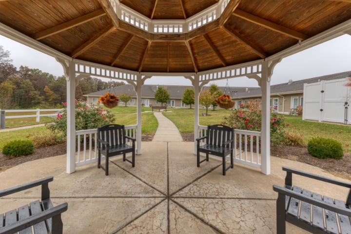 A wooden gazebo with benches overlooks a garden and pathway in an outdoor setting.
