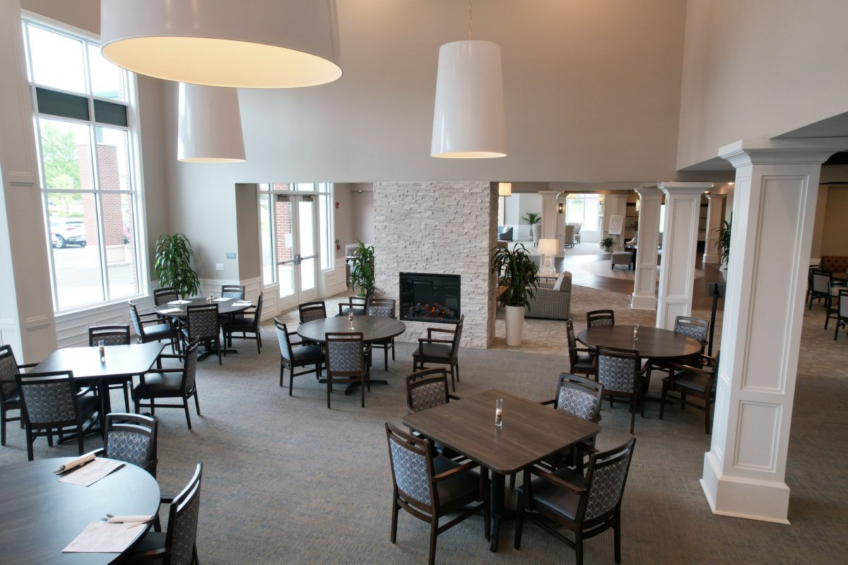 A spacious dining area featuring multiple tables and chairs, large pendant lights, and a central fireplace.