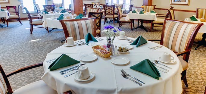 A neatly set dining table in a restaurant with green napkins and elegant decor.