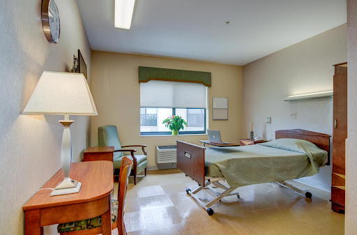 A well-lit hospital patient room featuring a bed, seating area, and window.