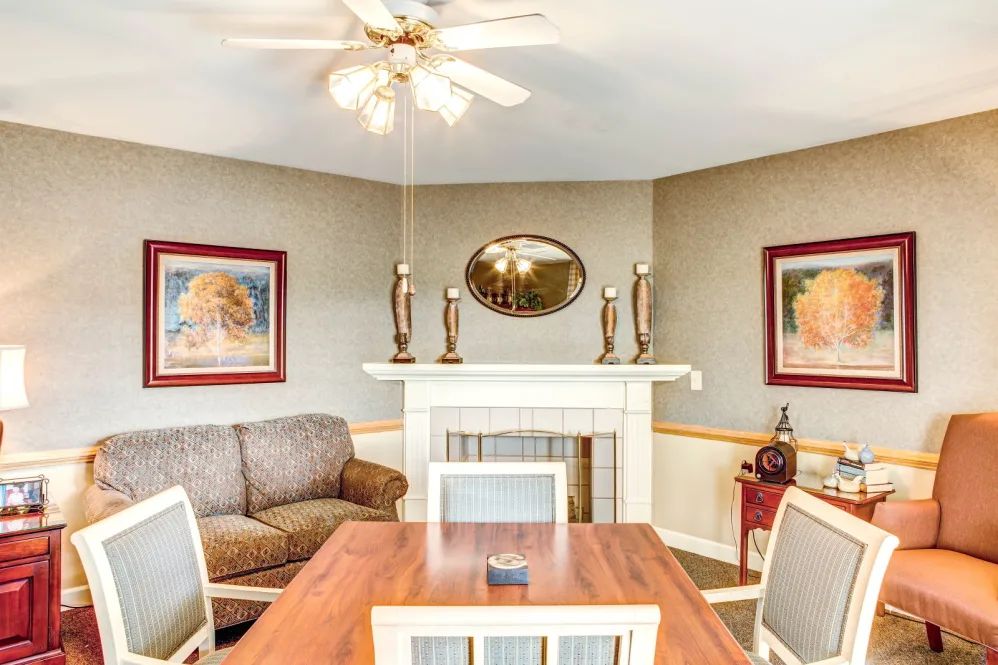 A cozy living room with a combined dining area featuring a wooden table, comfortable sofa, and decorative fireplace adorned with candles and artwork.