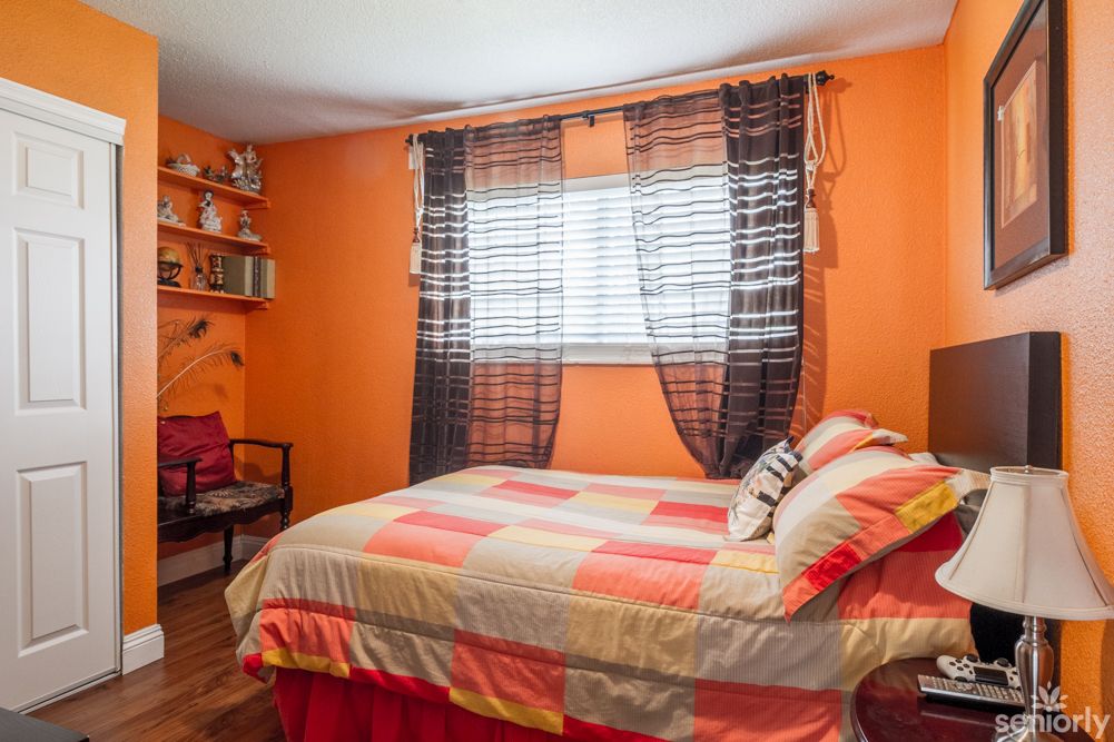 A cozy bedroom with vibrant orange walls and a neatly made bed.