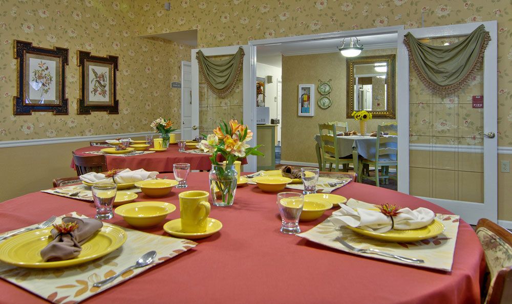 A warmly decorated dining room with tables set for a meal, featuring yellow dishware and floral centerpieces.