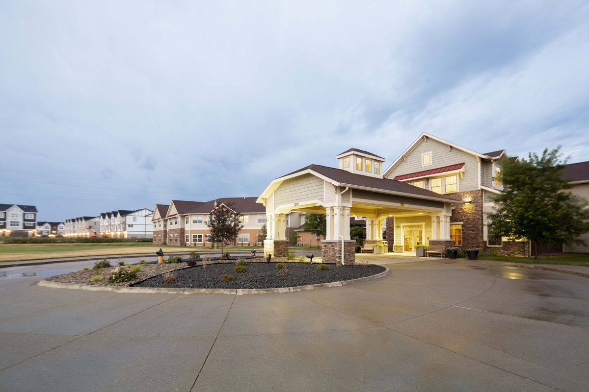 A well-lit building with a covered entrance and spacious driveway under a cloudy sky.