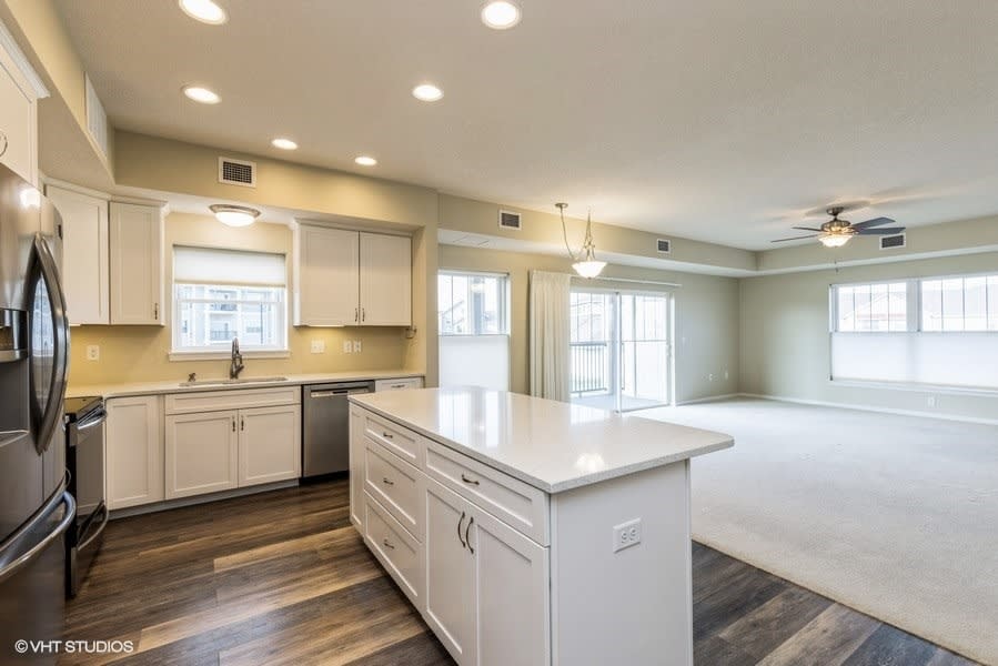 A modern kitchen with an open floor plan, featuring white cabinetry and a central island counter.